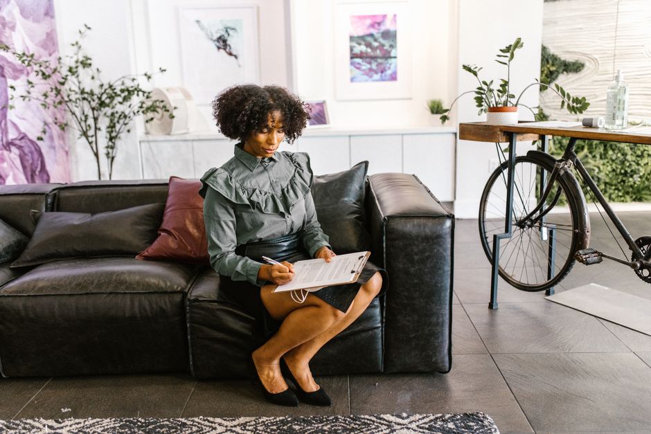 A professional woman with afro hair sits on a leather sofa reviewing documents in a modern, stylish office.