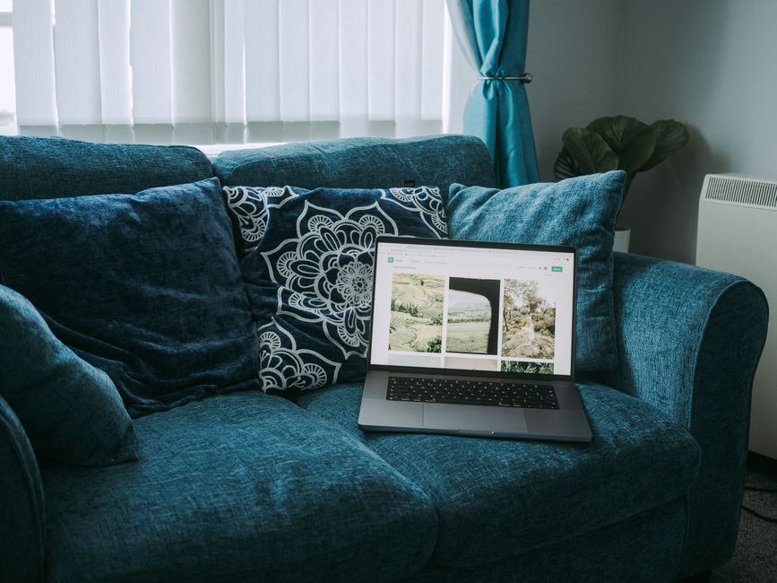 A sleek laptop on a plush blue sofa with decorative pillows, showcasing a calm and modern home interior.