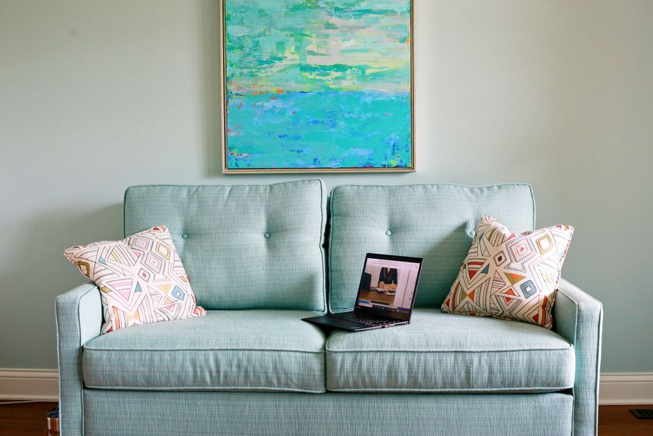 Stylish teal sofa with geometric pillows and a laptop, complemented by abstract wall art.